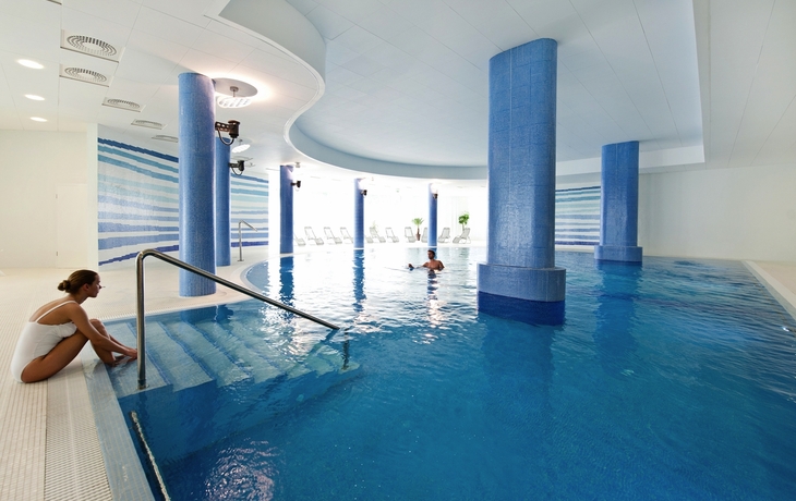 Ein modernes Hallenbad mit blauen Fliesen und einer Person im Wasser.