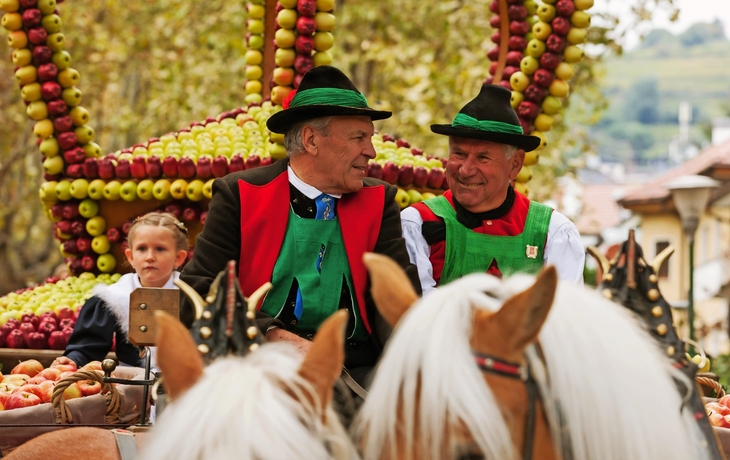 Männer in Tracht auf einem mit Äpfeln geschmückten Wagen beim Meraner Traubenfest.