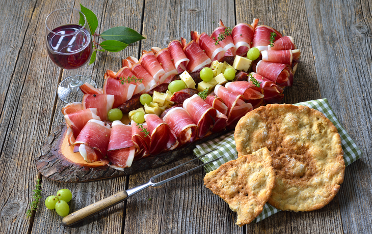 Wurstplatte mit Speck, Käse, Trauben und Brot auf Holztisch.