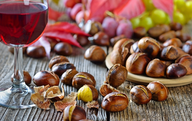 Geröstete Maroni mit Rotwein und Weintrauben auf Holztisch.