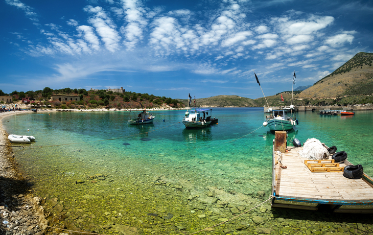 Klüre Bucht mit Booten und Anlegestelle bei klarem, türkisfarbenem Wasser und bewölktem Himmel.