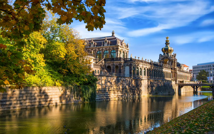 Zwinger in Dresden mit Kronentor und Langgalerien, umgeben von Wasser und Herbstbäumen.