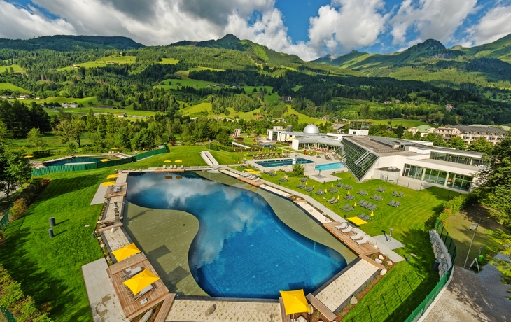 Thermalbadesee mit grüner Landschaft und Bergen im Hintergrund.