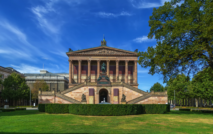 Alte Nationalgalerie in Berlin mit blauen Himmel und umgebenden Bäumen im Vordergrund.