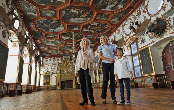 Besucher im Rittersaal von Schloss Weikersheim mit verzierter Kassettendecke.